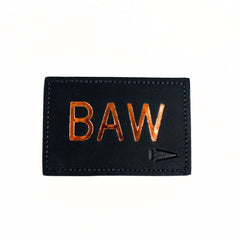 The Patch - Custom Leather Monogram features a black leather patch with shiny gold "BAW" letters and a small gold arrow, making it a unique personalized gift, shown on a crisp white background.