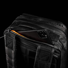A black smartphone partially inside the front zip pocket of the GR2 USA x Carryology - Ultra Black backpack, crafted from Challenge Sailcloth UHMWPE fabric, set against a black background.