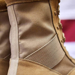 Close-up of the MACV-1 Hi-Speed - High Top boot from GORUCK, showcasing its detailed stitching and rugged fabric while meeting AR670-1 compliance standards. The lightweight rucking boot is laced up tightly, emphasizing its durable build. A blurred red and white background adds depth to the image, enhancing its military-ready appeal.