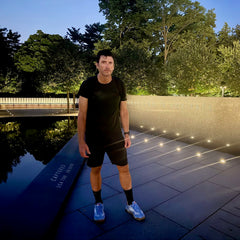 Wearing the Mackall 45 Americana, a man in a black outfit stands beside an illuminated memorial wall at night, where the words “FREEDOM IS NOT FREE” can be seen.