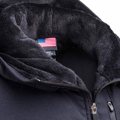 A close-up of the GORUCK Vest of Power - ToughDry® + Fleece in black, showcasing its cozy, soft inner lining. The zipper is partially open, revealing an American flag tag along with a care label inside. The texture of the lining looks plush and warm, reflecting an environmentally conscious design approach.