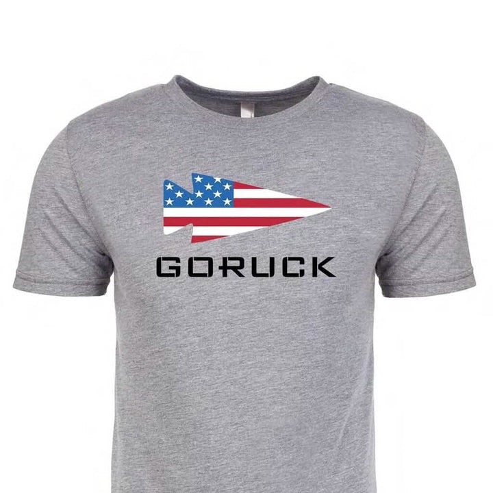 The GORUCK USA Tee - Tri-Blend is a grey T-shirt with a spearhead arrow-shaped American flag above bold "GORUCK" text, crafted from premium tri-blend fabric for superior comfort and durability.