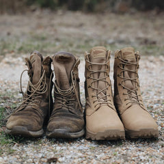 Two pairs of boots rest side by side on a gravel path. The pair on the left is worn and scuffed, while the pair on the right looks like GORUCK's MACV-2 - High Top in Coyote, featuring a triple compound outsole and appearing new and clean. Both are in a similar tan color, with grass visible in the background.