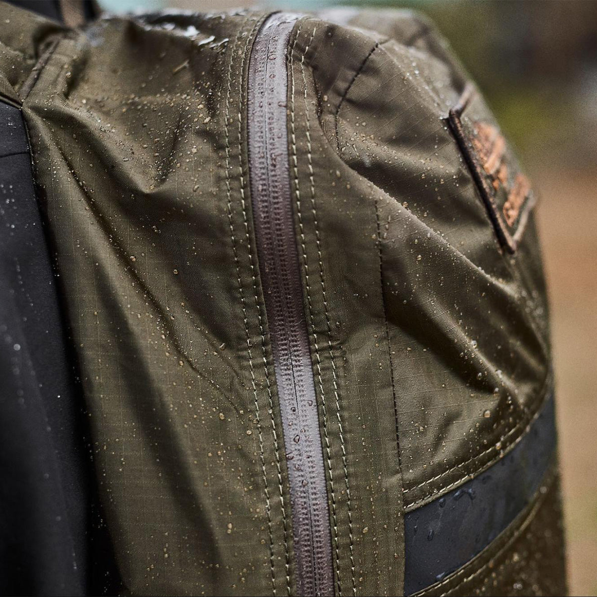 Close-up of a green waterproof backpack with raindrops on the fabric and zipper.