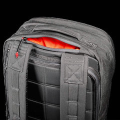 A close-up of a black GORUCK GR2 - Cordura backpack shows an open zipper revealing its orange interior. Inspired by Special Forces design, this backpack features padded shoulder straps and a grid pattern on the back, with zippers that have small red tab accents.