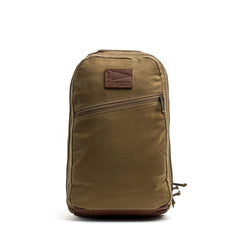 The Double Compartment Bullet Ruck - Heritage Waxed Canvas - 18L features a tan waxed canvas build, front zipper pocket, and a brown leather patch logo—ideal for use as a durable travel daypack.