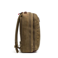 The Double Compartment Bullet Ruck - Heritage Waxed Canvas - 18L is a brown waxed canvas backpack with padded straps and multiple zippered compartments, shown from the side—ideal as a durable travel daypack.
