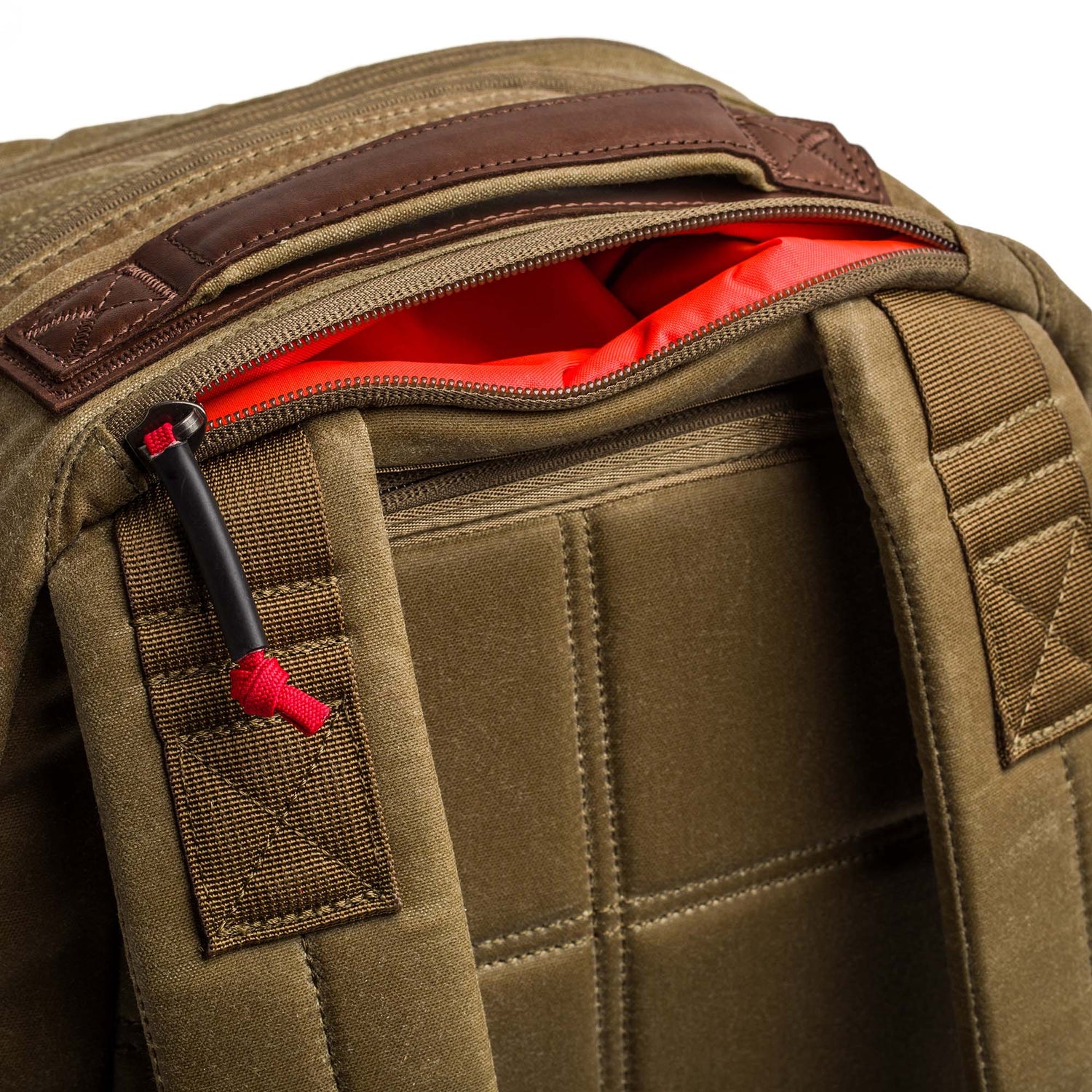 Close-up of the Double Compartment Bullet Ruck - Heritage Waxed Canvas - 18L, featuring padded straps and a khaki waxed canvas exterior with a zippered pocket lined in bright red fabric.