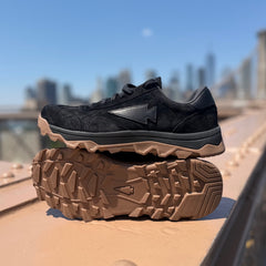 Mackall 45 Black + Gum sneakers with brown rugged soles displayed outdoors on a bridge with a city skyline in the background.