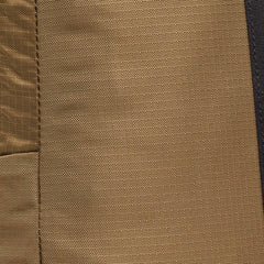Close-up of brown textured fabric with visible stitching on a Basic Rucker® backpack, featuring a dark vertical strip on the right side.