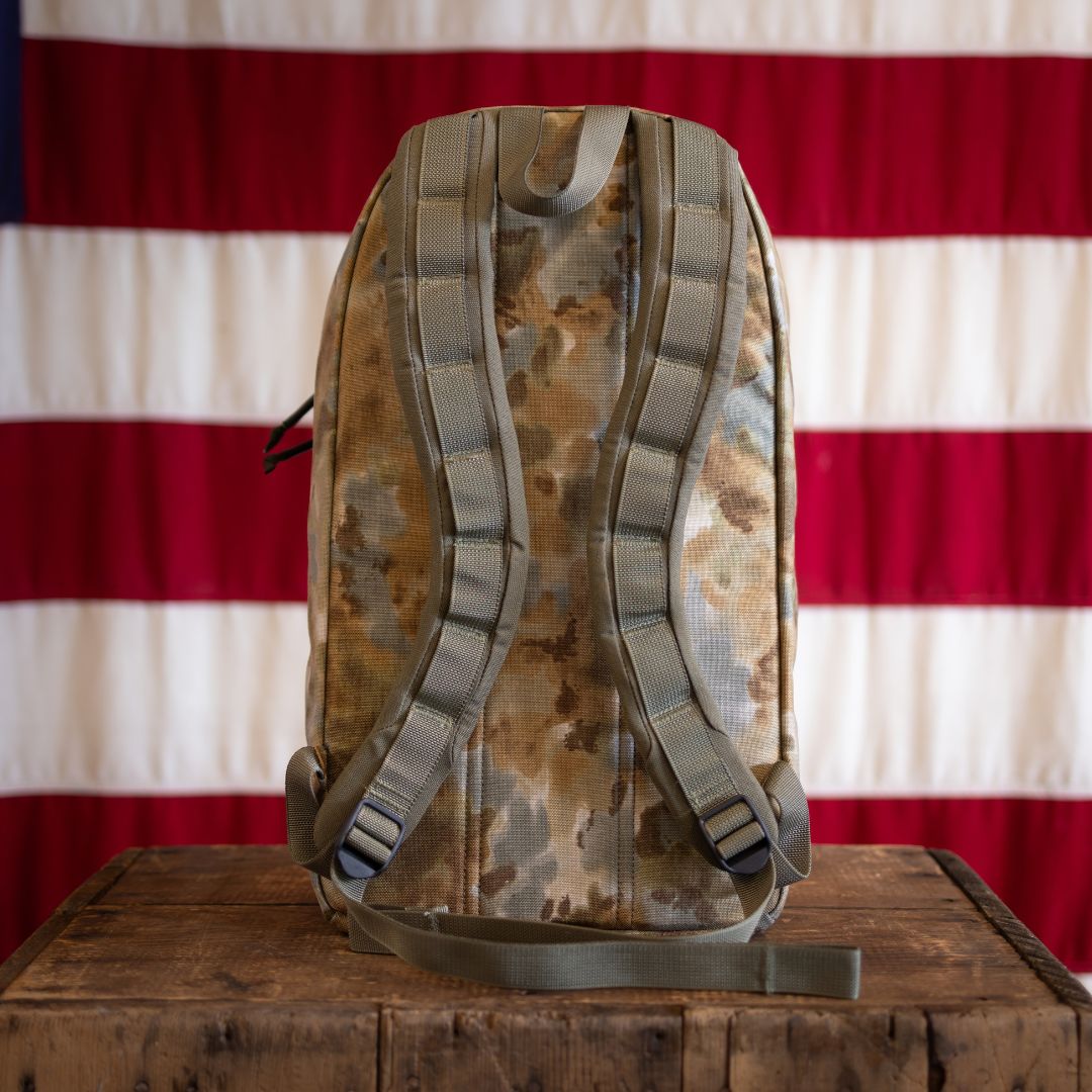 An Arid Bullet - Built by Scars backpack rests on a wooden box with an American flag in the background.