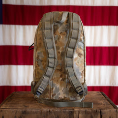An Arid Bullet - Built by Scars backpack rests on a wooden box with an American flag in the background.