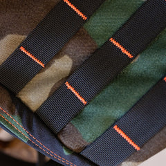 Close-up of a limited edition camouflage fabric with black webbing straps secured by bright orange SCARS cross-stitching.