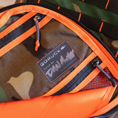 Close-up of a limited edition camouflage backpack interior, featuring an orange-trimmed zippered pocket with a GORUCK logo patch.
