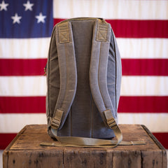 Limited edition grey backpack with adjustable shoulder straps and a custom barbed wire design sitting on a wooden crate in front of an American flag.