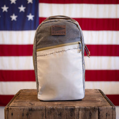 A two-tone, limited edition GORUCK backpack with a leather logo patch sits on a wooden crate in front of an American flag.