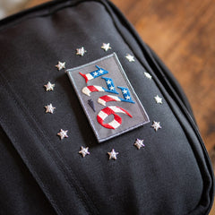 13 Stars GR1 21L - Built by Scars: black backpack with “USA” patch and silver stars, classic rucksack style.