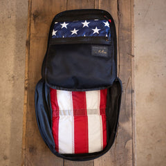 An open Fireworks GR1 21L - Built by Scars on a wooden table holds a folded American flag inside.