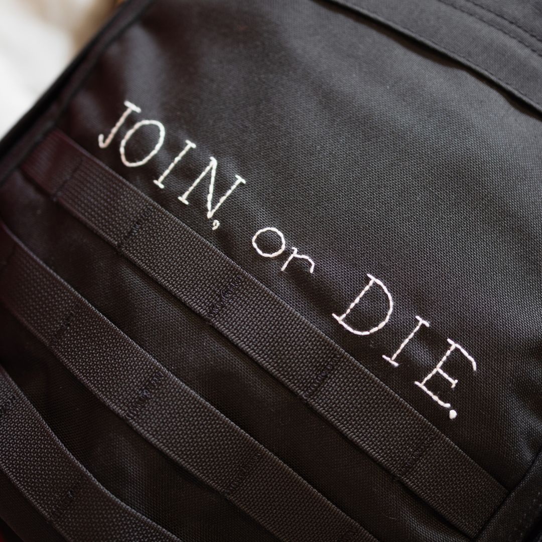 Black bombproof Cordura with white “JOIN, or DIE.” text on the Join or DIE GR1 21L - Built by Scars.