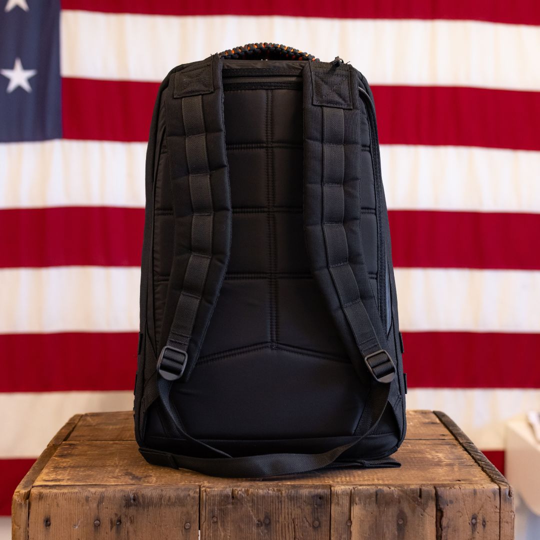 Back view of a limited edition GR1 rucksack with padded shoulder straps sitting on a wooden crate in front of an American flag.