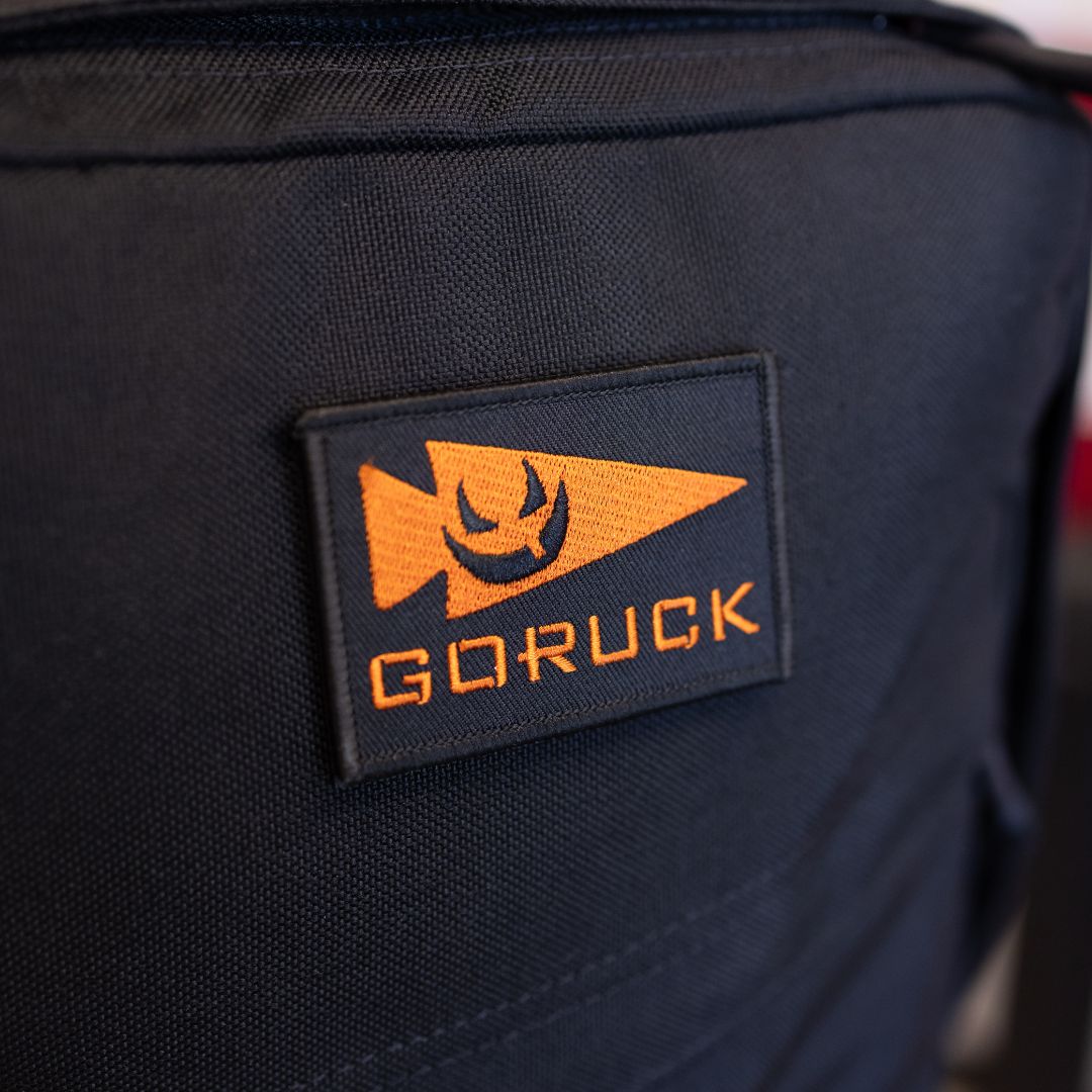 Black limited edition GR1 rucksack featuring an orange patch with a spearhead icon and a smiling face.