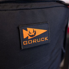 Black limited edition GR1 rucksack featuring an orange patch with a spearhead icon and a smiling face.