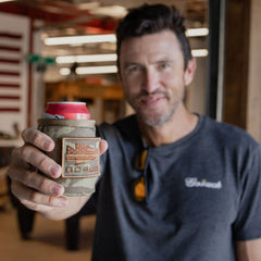 A man holds a canned drink in a camouflage GORUCK Ballistic Beer Jacket with an arrowhead design, which keeps his drink cold.