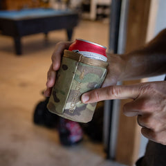 A person holds a beverage can in a camouflage-patterned GORUCK Ballistic Beer Jacket that keeps the drink cold.