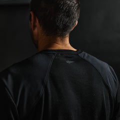 Close-up of a man’s back wearing the Men’s Commando Tee - Merino Wool in black, featuring reinforced shoulders. His short dark hair stands out against the dark background.