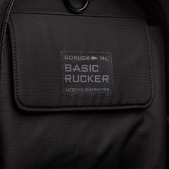 Close-up of the Basic Rucker backpack in black, showcasing its pocket and label reading "GORUCK 14L BASIC RUCKER LIFETIME GUARANTEE." Designed for rucking, this pack securely holds your ruck plate.