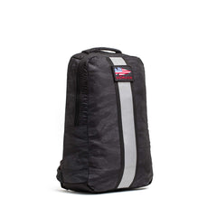 The Basic Rucker is a black backpack with a gray reflective stripe, top handle, and an American flag patch with "GORUCK" text—ideal for daily adventures.
