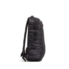 Side view of the Basic Rucker, a black backpack with a zipper and adjustable shoulder straps, shown against a white background.