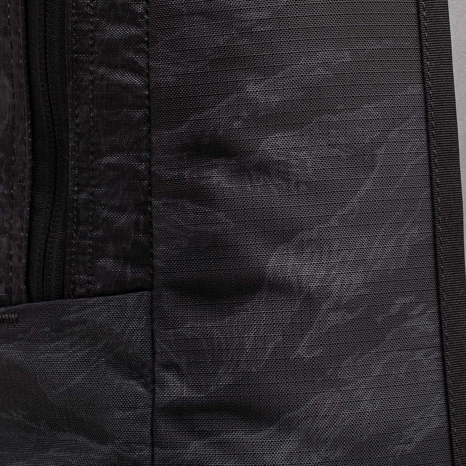 Close-up of the Basic Rucker's black textured fabric with a left-side zipper, highlighting the backpack's durable material.