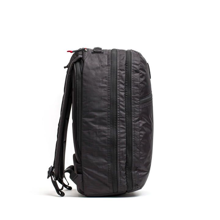 The GORUCK Bullet Ruck Double Compartment, made from durable Dyneema, is displayed in profile against a white background. It boasts a sleek design with multiple zippers, adjustable shoulder straps, and a sturdy top handle, all backed by a lifetime guarantee for enduring quality.