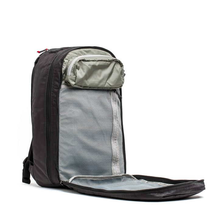 A GORUCK Bullet Ruck Double Compartment in black is open, showcasing its main section lined with a gray mesh pocket along with an extra small zippered pocket inside. Constructed from robust Dyneema fabric, it features a sleek, contemporary design equipped with a visible zipper and adjustable straps, all supported by a lifetime guarantee.