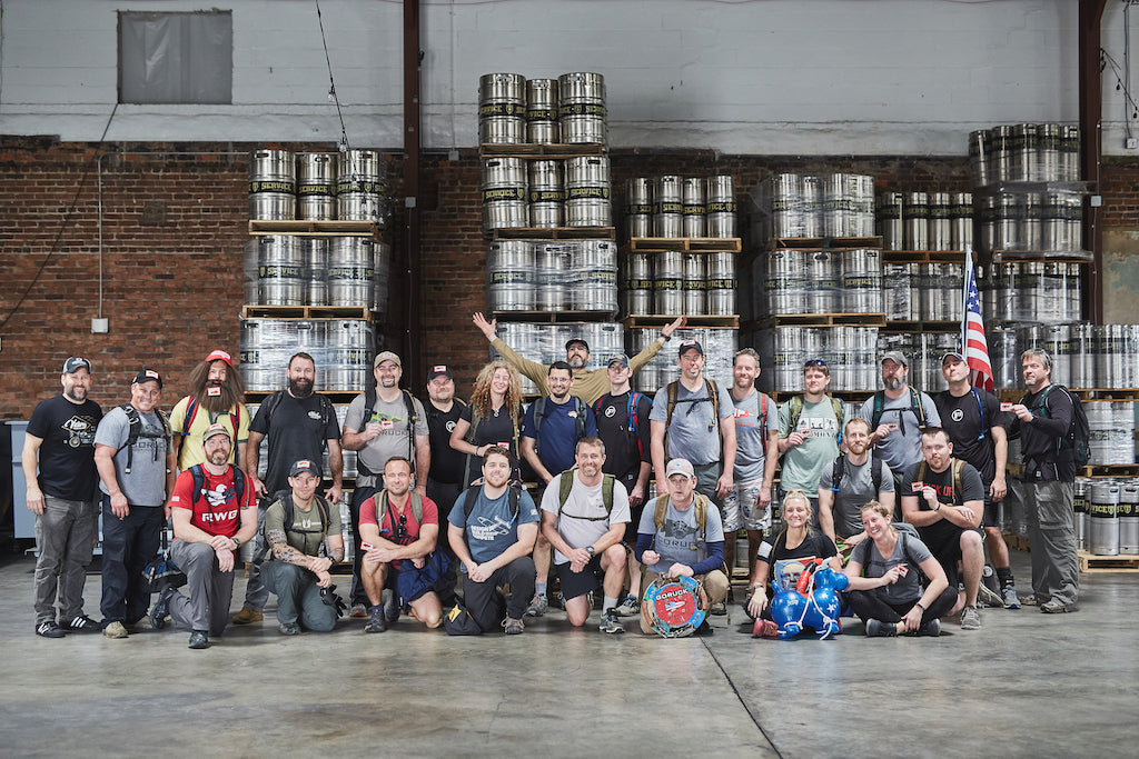 A group of people posing together in front of stacked beer kegs inside a warehouse.