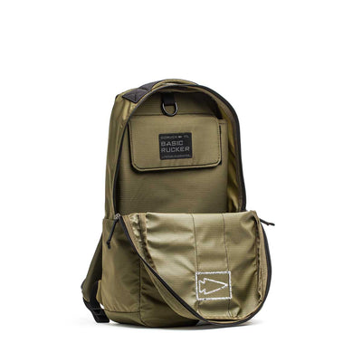 The Basic Rucker® backpack in olive green features a front zipper pocket that's partially open, revealing the main compartment.