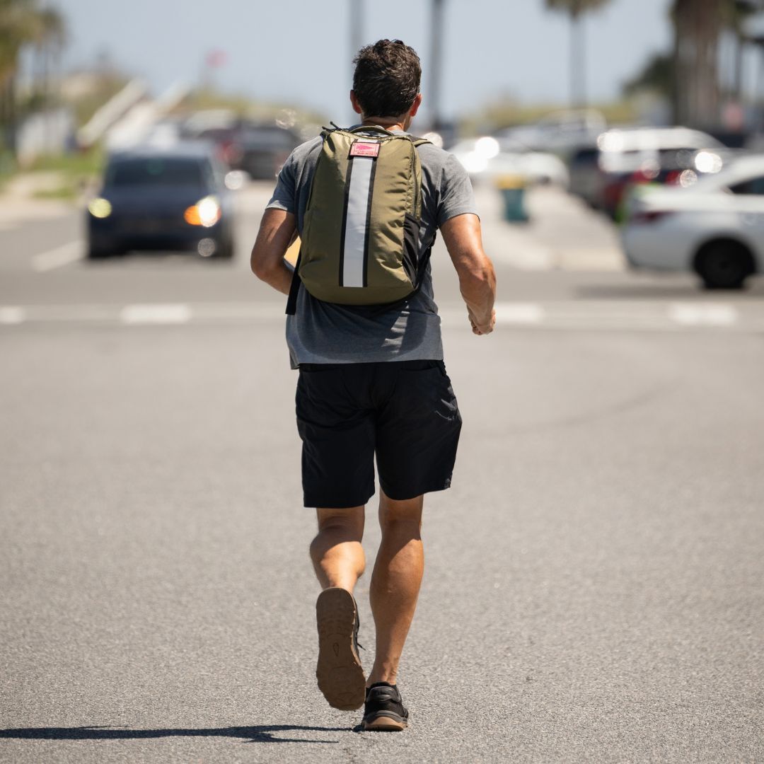 Wearing Merino Challenge Socks - Ankle (No-Show), a man with a backpack runs down a sunny street toward parked cars and distant palm trees.