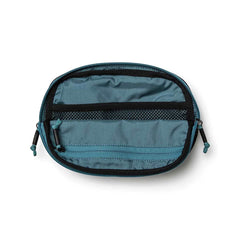 A compact belt bag from GORUCK, crafted from blue Cordura, showcases an oval shape with black trim and zippers. Inside, you'll find a black mesh pocket. The pouch features zipper handles on both ends and appears empty while laid flat.