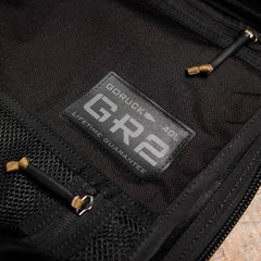 A close-up of a black backpack's interior reveals a patch displaying the text "GORUCK GR2 40L LIFETIME GUARANTEE." Created with the same durability as those used by Special Forces, this travel bag features robust material, strong zippers, and convenient mesh pockets.