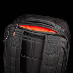 Close-up of a GR2 travel bag by GORUCK against a dark background, showcasing its detailed stitching and padded straps. The top zipper is partially open, revealing a bright orange interior lining.