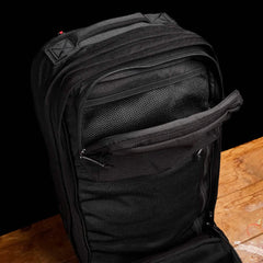The GR2 travel bag by GORUCK is open on a wooden surface, revealing several compartments and zippers. It seems to be crafted from durable fabric with mesh sections for organization. The background is a plain black.