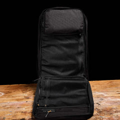 A black GR2 travel bag from GORUCK, similar to those used by Special Forces, rests on a wooden surface against a dark background. Its open design reveals mesh compartments, highlighting an interior ideal for efficient packing.