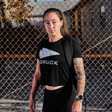 Woman wearing black GORUCK crop top and backpack in front of a chain-link fence outdoors
