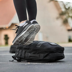 Person stepping on GORUCK black rucksack outdoors, wearing athletic shoes and leggings