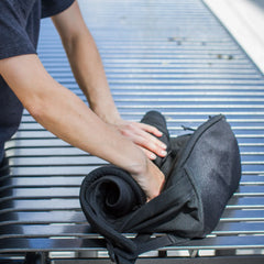 Person packing black GORUCK rucksack on outdoor metal bench