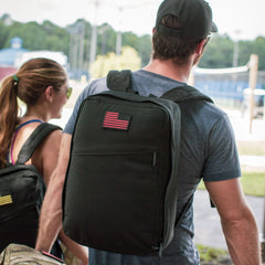 Man wearing GORUCK black rucksack with USA flag patch outdoors, rucking gear showcased