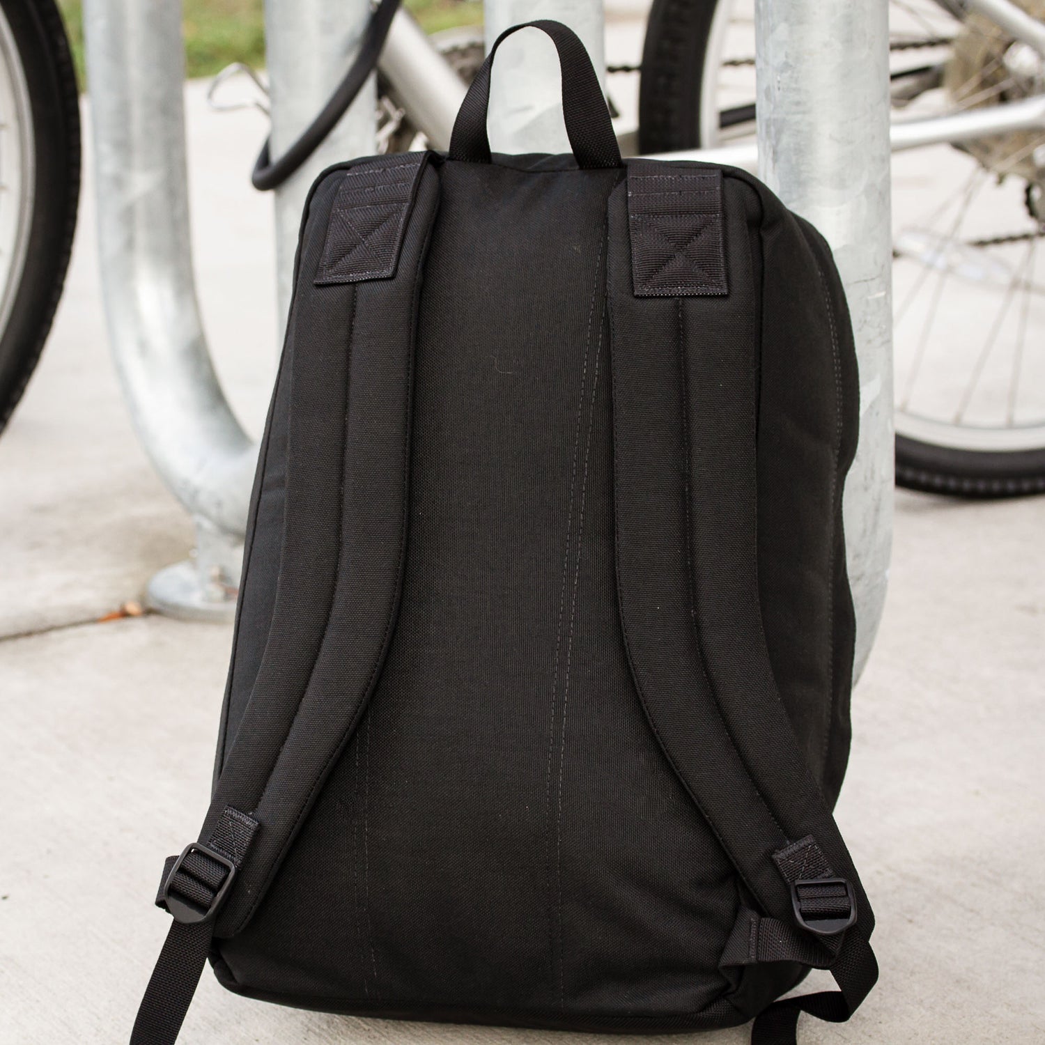 The Shadow Ruck—a lightweight, durable backpack—rests by a bike rack with two bicycles in the background, making it perfect for your everyday carry needs.