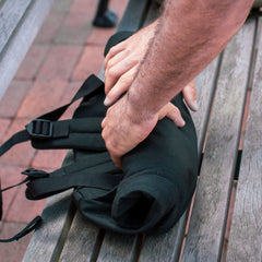 Hands rolling up a black GORUCK rucksack on a wooden bench outdoors