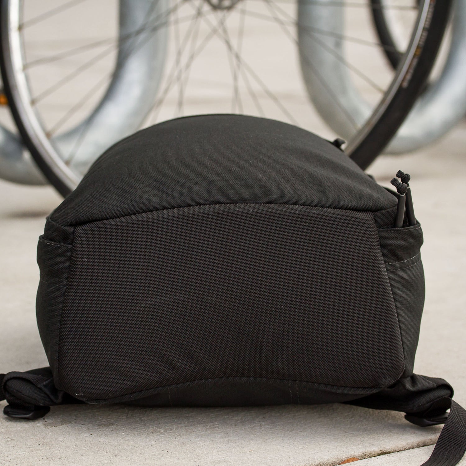 The Shadow Ruck, a lightweight backpack, rests on the ground in front of a bicycle wheel—ideal for everyday carry.
